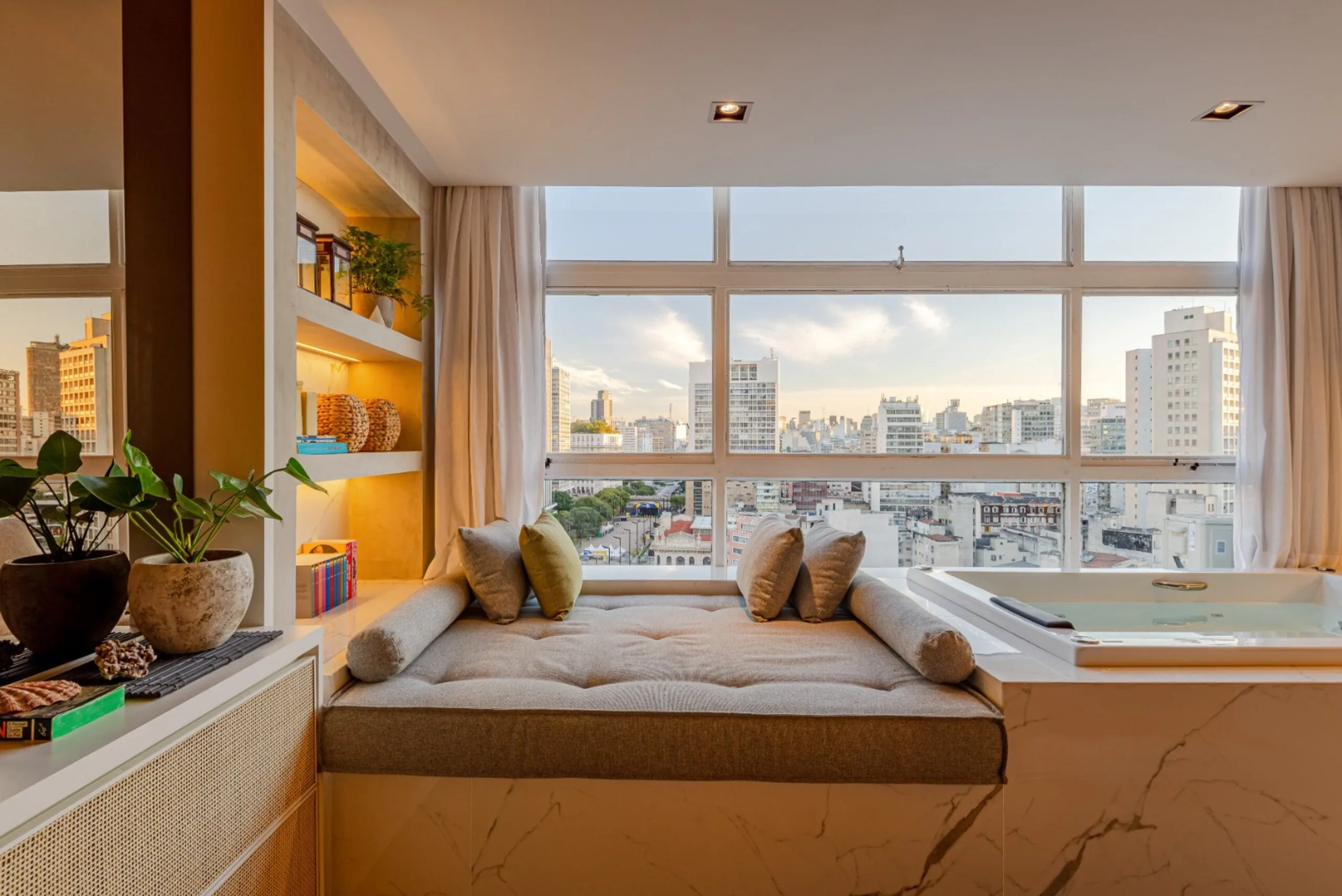 Sala de estar integrada com vista panorâmica da cidade, equipada com banheira de hidromassagem, ar-condicionado, smart tv 85" c/ streaming, cortinas blackout, sistema de som e livros com material de leitura.