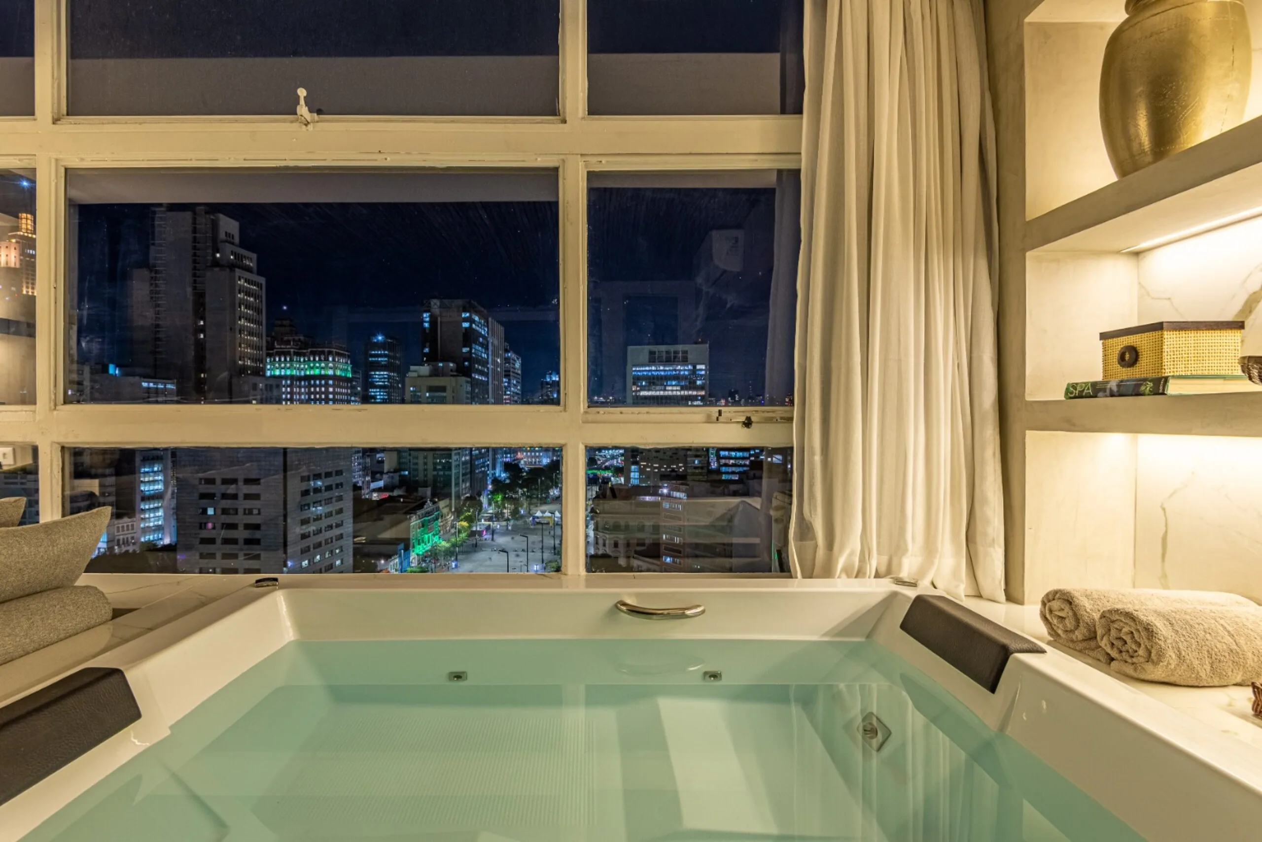 Banheira de SPA de casal localizada no quarto, integrada à sala de estar e com ampla vista para a cidade.